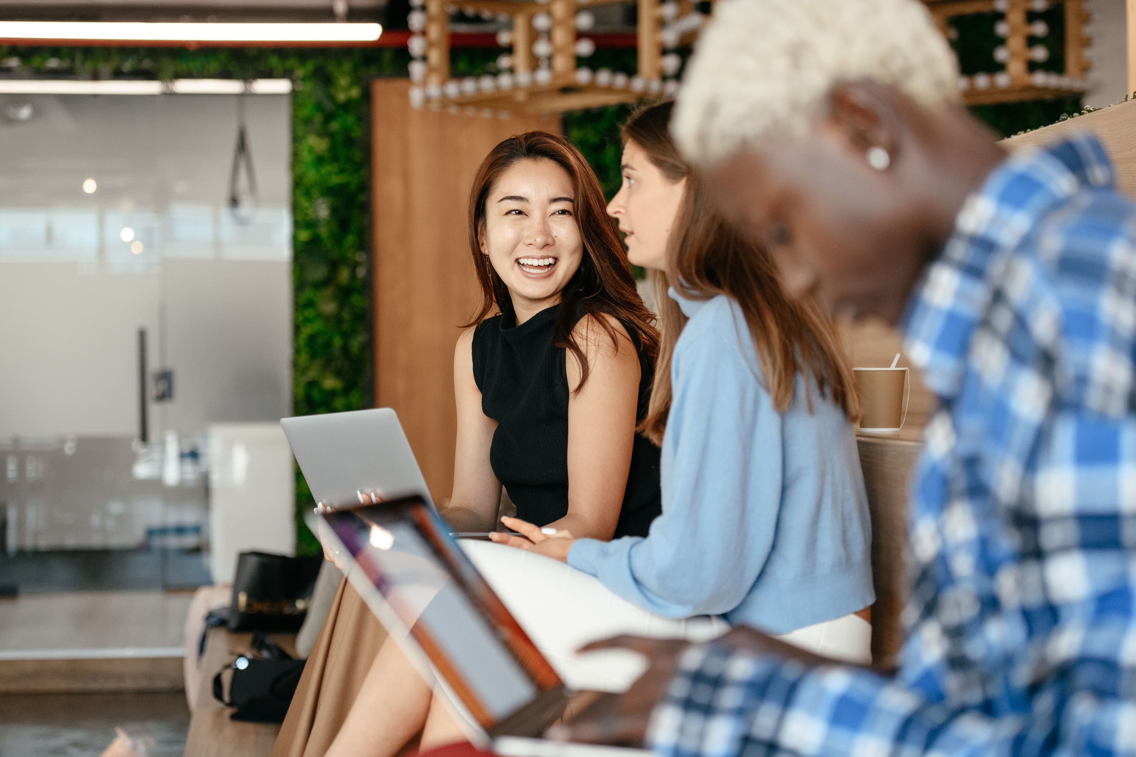 A group of diverse professionals engaging in conversation and work on laptops in a modern office setting